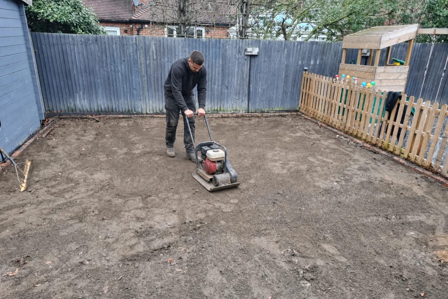 Installer compacting the sub-base with a plate compactor before the grass goes down