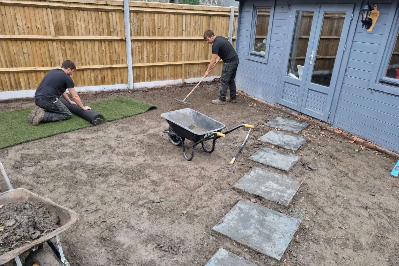Installers rolling out artificial grass over a prepared sub-base in a British back garden